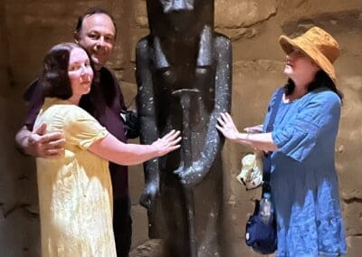 Three people gather around and touch the powerful black granite statue of Sekhmet at Ptah Temple, Karnak